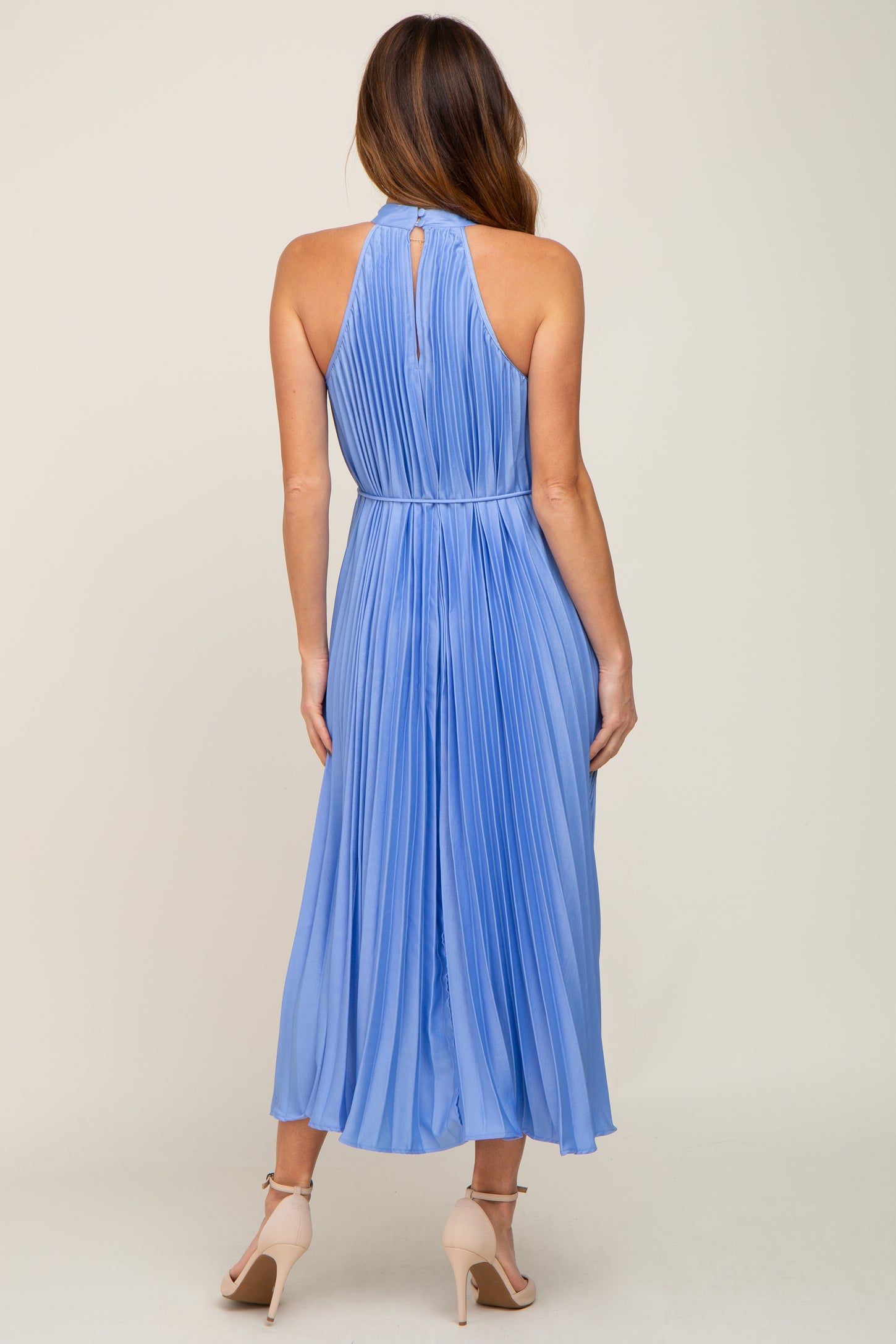 woman wearing a light blue pleated halter neck midi dress, showing the back view and a flowing silhouette