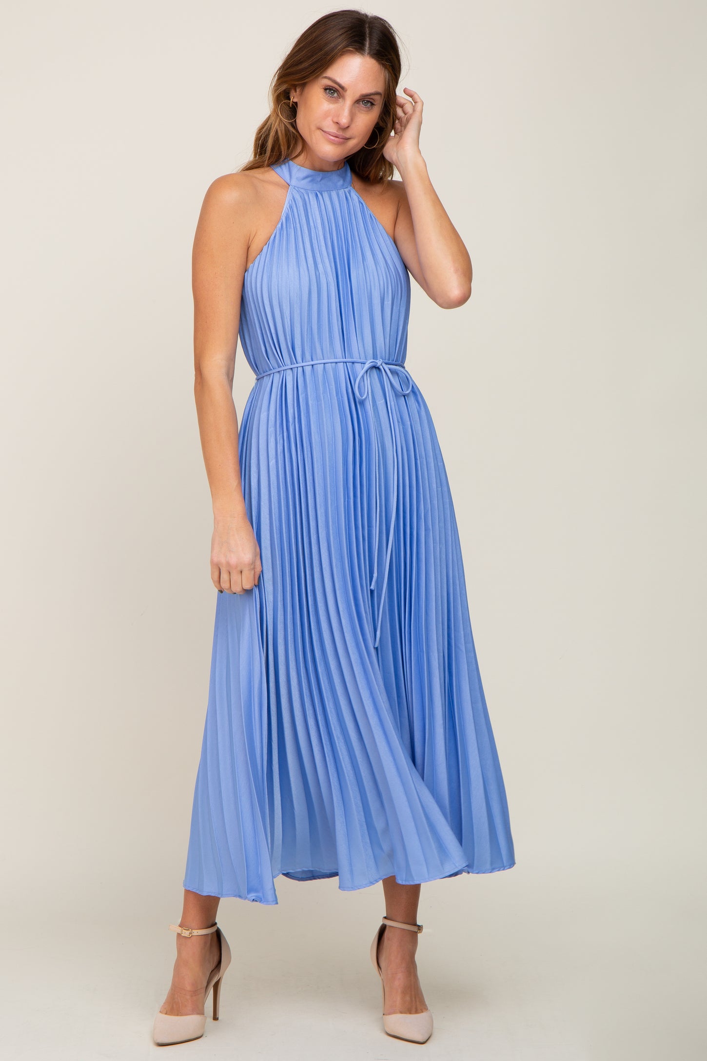 woman wearing a pleated halter neck midi dress in light blue with a tie waist