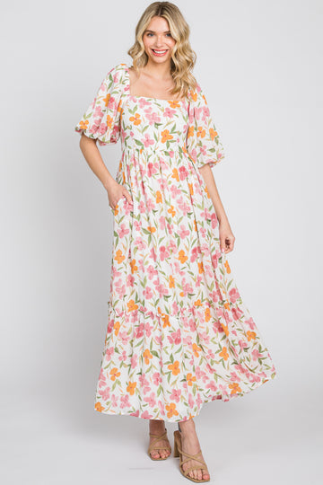 woman wearing a floral maxi dress with puff sleeves and pockets in pink, orange, and green colors