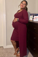 woman wearing a burgundy maternity dress with a long cardigan, holding her baby bump and smiling