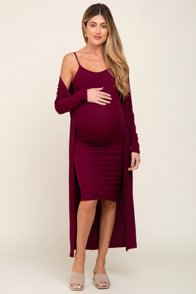 woman wearing a burgundy ribbed maternity dress with a matching long cardigan and holding her baby bump