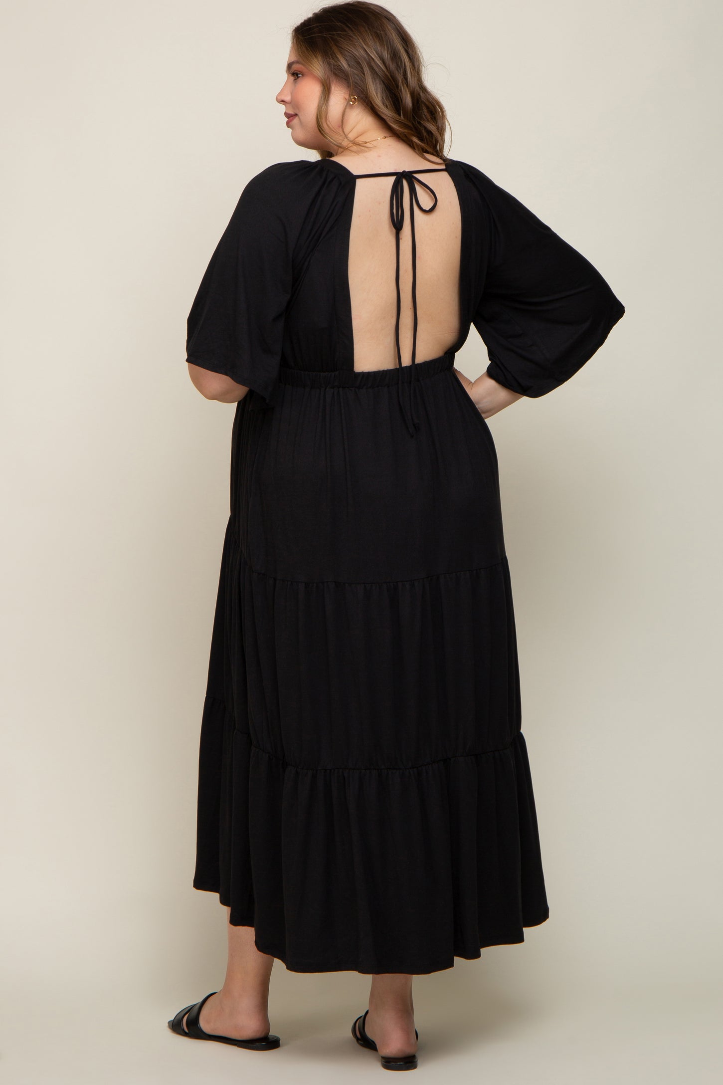 maternity plus size woman wearing a backless black tiered maxi dress with a tied closure at the back