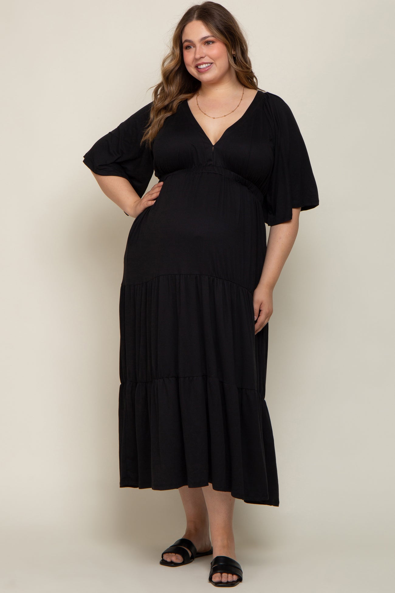 woman wearing a black maternity plus maxi dress with a v-neckline and flutter sleeves, styled with flat sandals