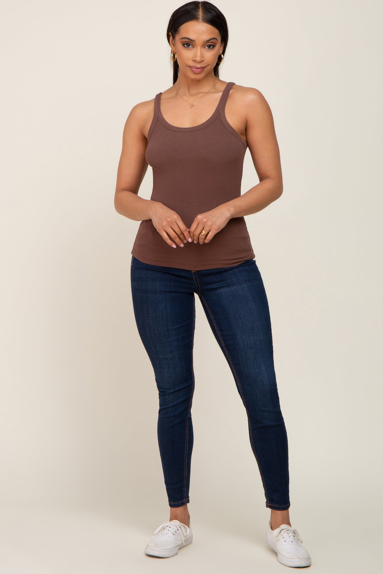 woman wearing a brown ribbed tank top paired with blue skinny jeans and white sneakers