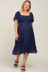 woman wearing a navy blue maternity plus dress with short puff sleeves and a smocked bodice, showcasing her baby bump
