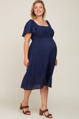 pregnant woman wearing a navy blue smocked maternity midi dress with flutter sleeves and brown heels
