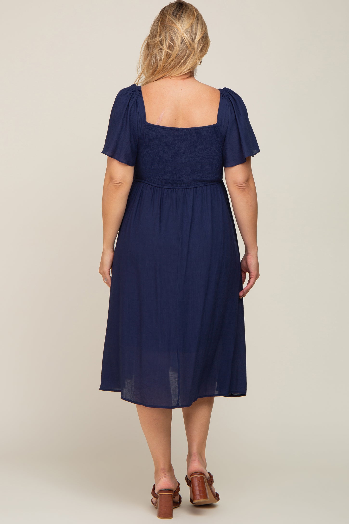 woman wearing a navy blue maternity plus dress with short puff sleeves and a smocked bodice, viewed from the back