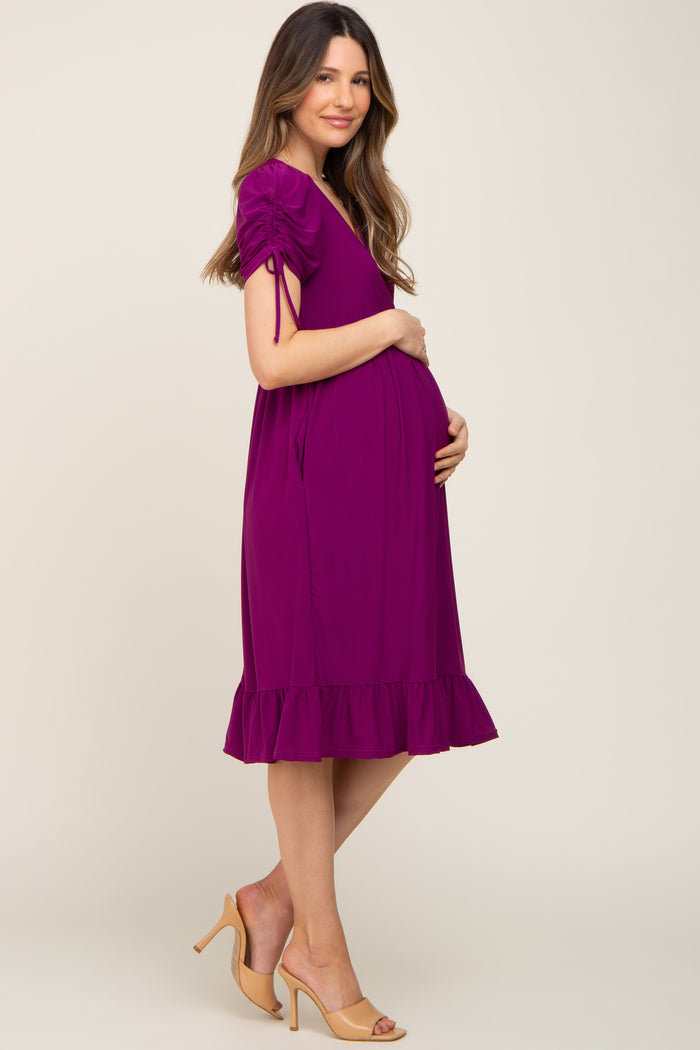 woman wearing a purple maternity dress with short puff sleeves and ruffled hem, cradling her baby bump