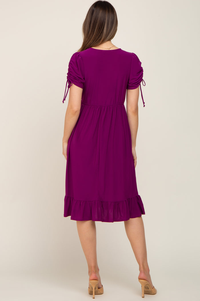 woman wearing a purple maternity dress with puff sleeves and a ruffled hem, showing her baby bump