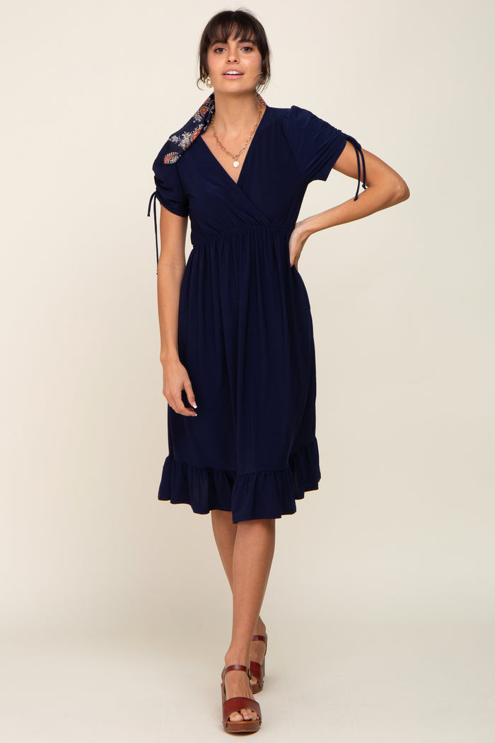 woman wearing a navy blue short sleeve wrap dress with ruffled hem and floral tie detail on the shoulder