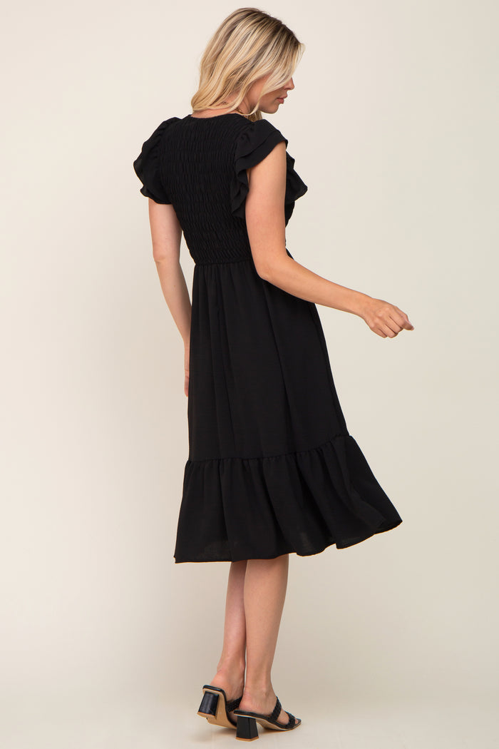 Woman wearing a black smocked midi dress with ruffle sleeves and a tiered hemline.