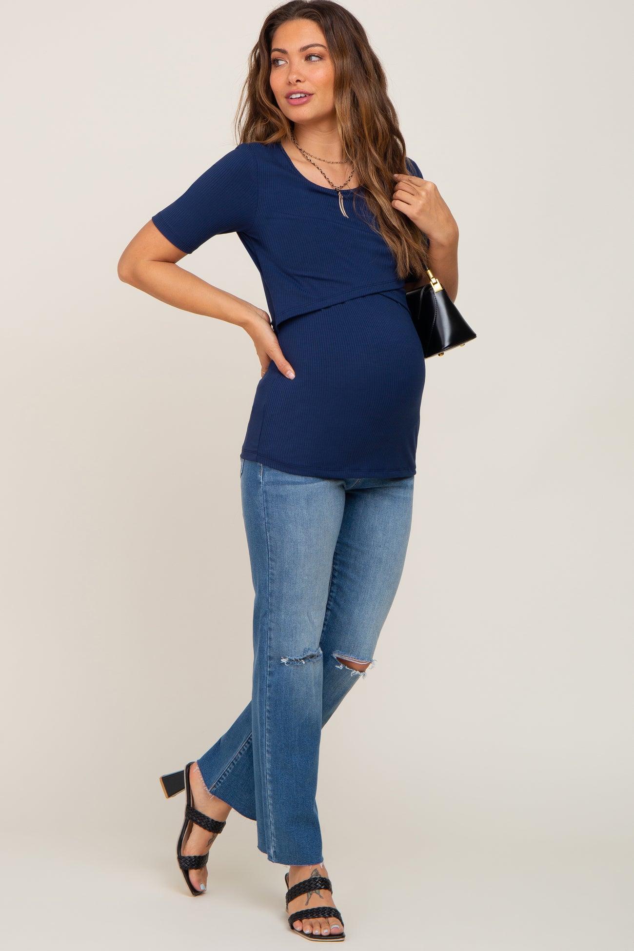 woman wearing a navy maternity top with a crossover design and blue distressed jeans, showcasing her baby bump