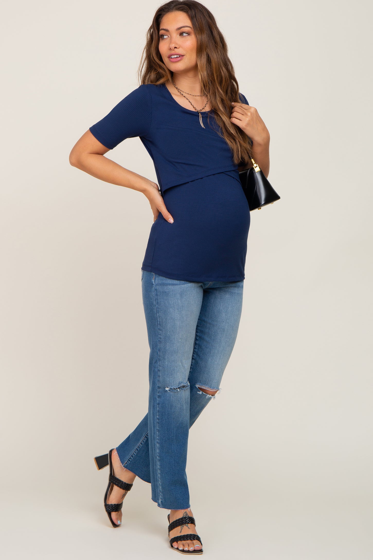 woman wearing a navy maternity top with a crossover design and blue distressed jeans, showcasing her baby bump