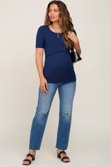 woman wearing a navy blue short sleeve maternity top with a baby bump and distressed jeans, holding a black handbag