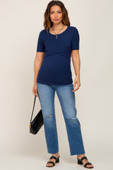woman wearing a navy short sleeve maternity top with a ruched waist and distressed blue jeans, holding a black handbag