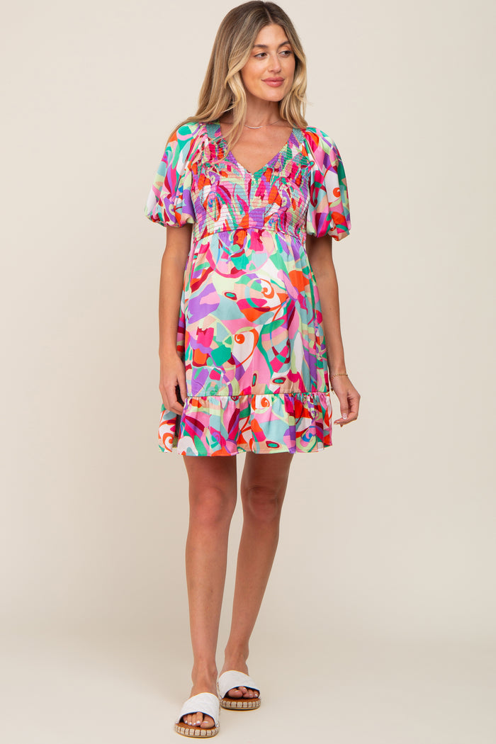 woman wearing a colorful abstract print maternity mini dress with smocked bodice and puff sleeves
