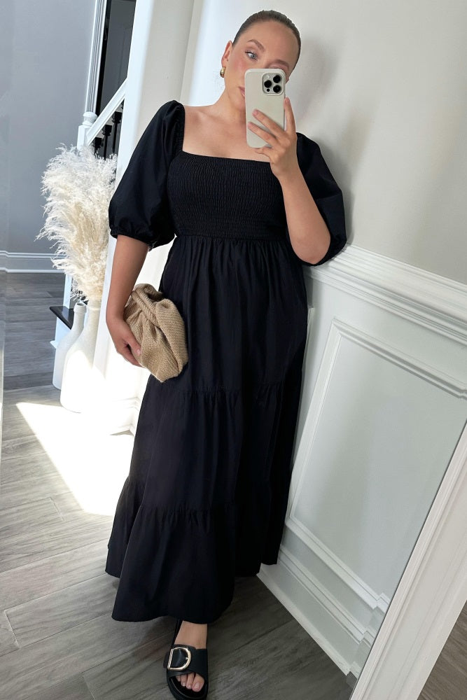 woman wearing a black smocked puff sleeve midi dress and holding a tan woven clutch bag
