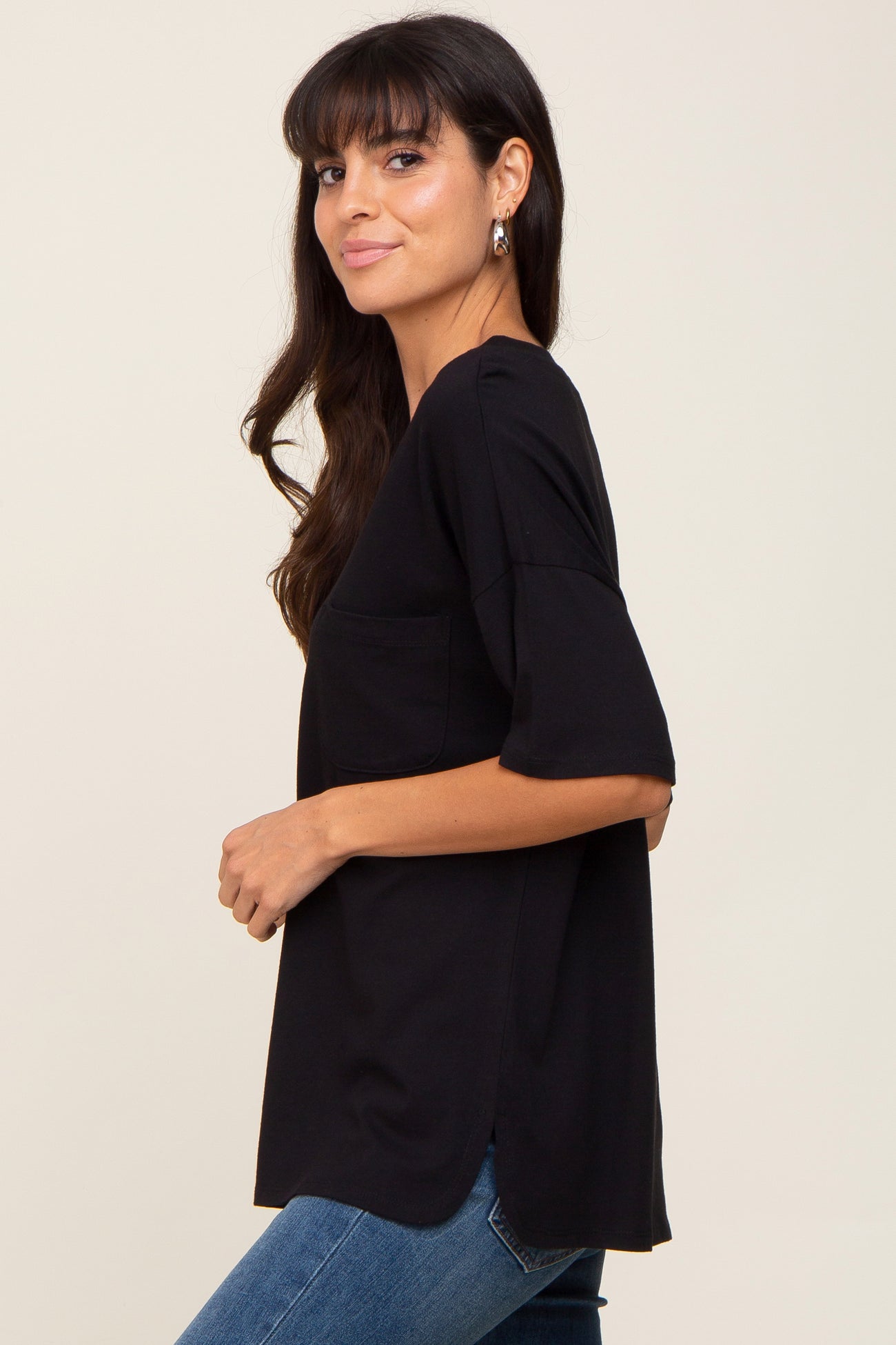 woman wearing a black short sleeve top with a front pocket and a loose fit, paired with blue jeans