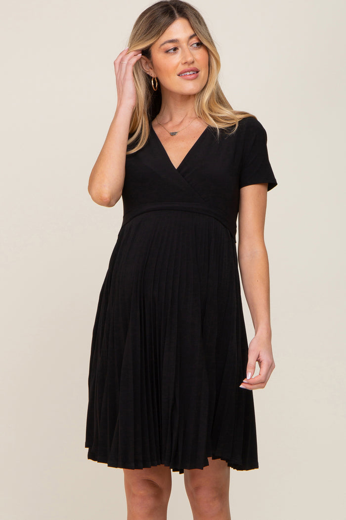 woman wearing a black pleated maternity dress with short sleeves and a v-neckline, highlighting her baby bump