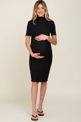 woman wearing a black ribbed maternity dress with short sleeves and scalloped edges, gently cradling her baby bump