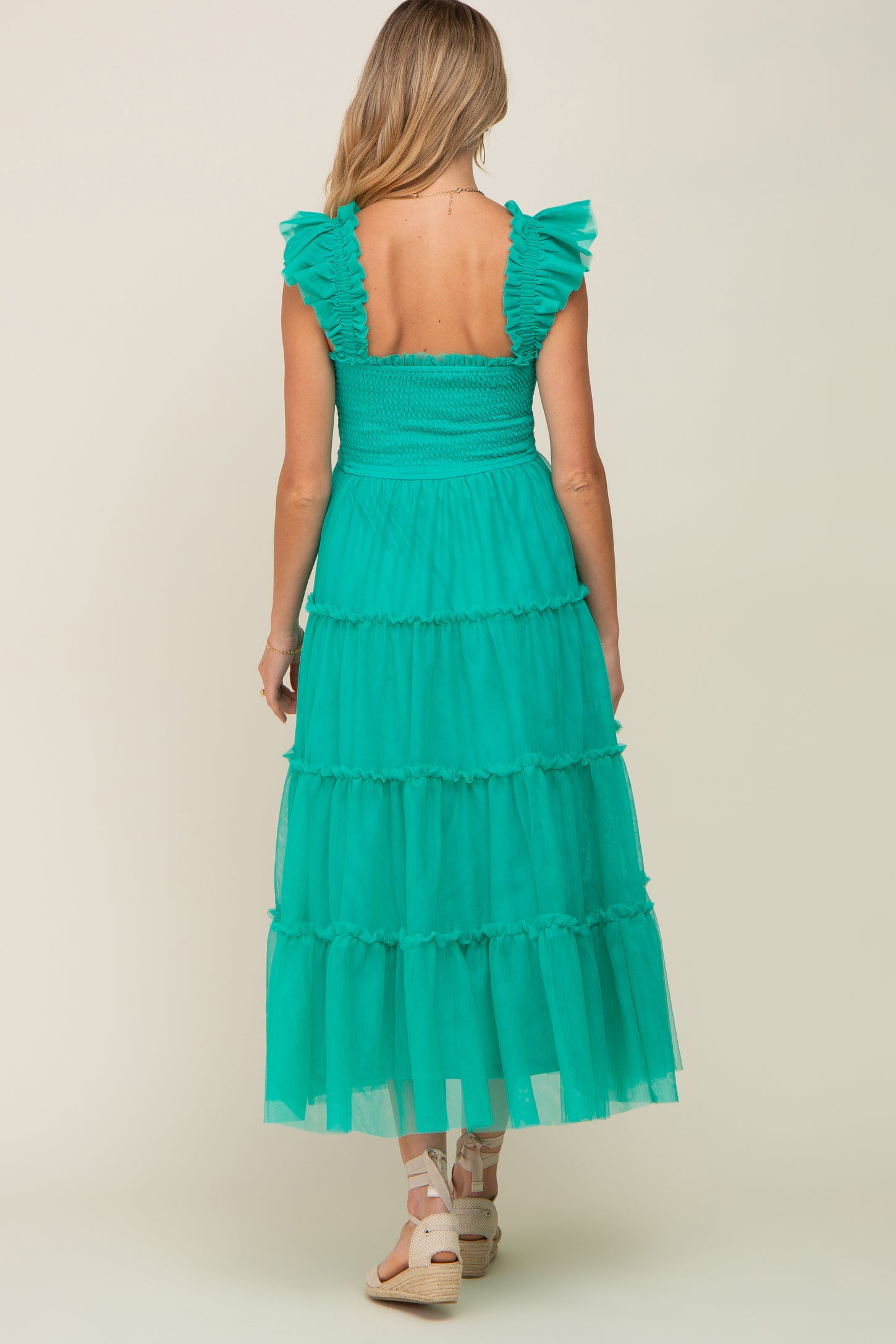 woman wearing a green tiered maternity dress with ruffled sleeves, showing the back view