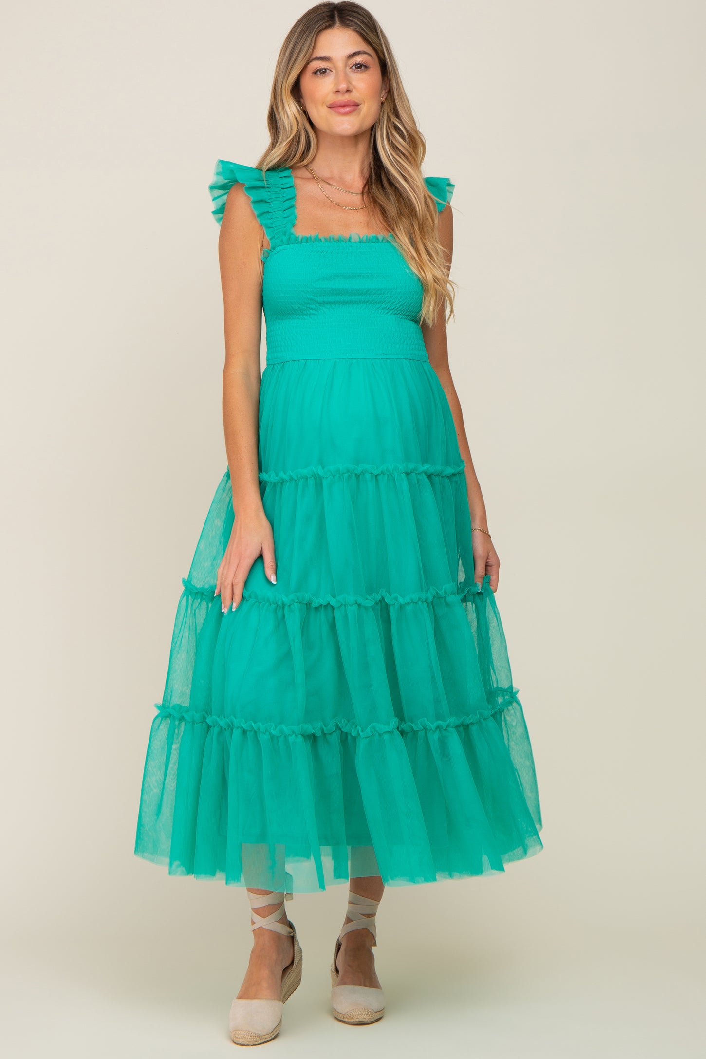 woman wearing a teal maternity dress with ruffled sleeves and tiered tulle skirt, showcasing her baby bump