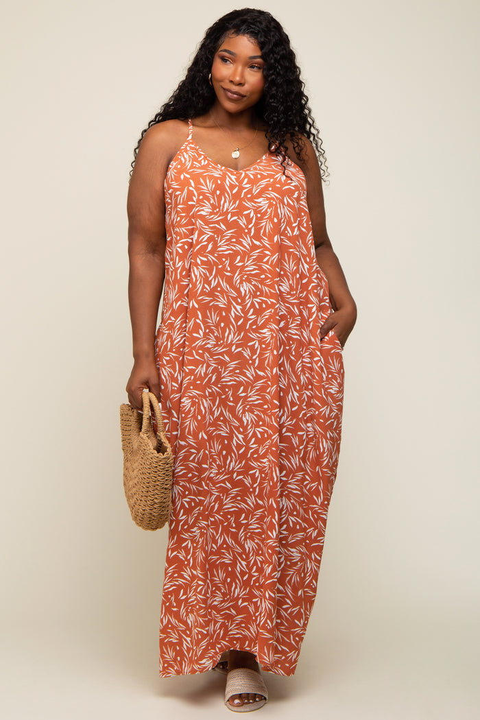 woman wearing an orange floral maxi dress with adjustable straps and side pockets, holding a woven bag