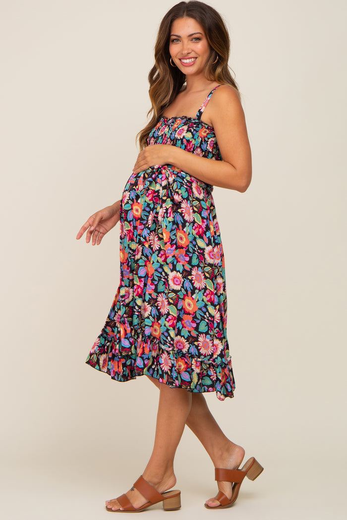 woman wearing a colorful floral maternity dress with adjustable straps and a ruffled hem, showing her baby bump