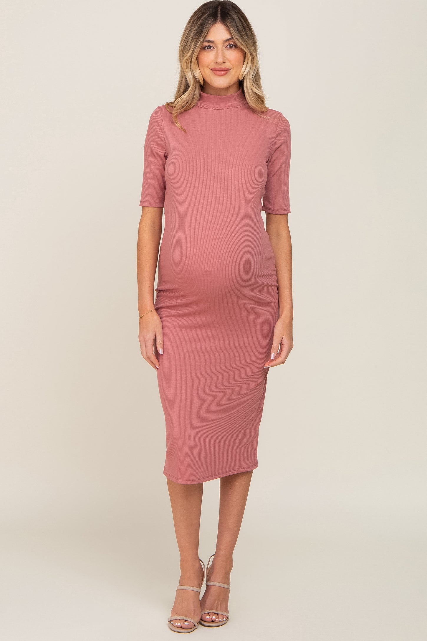 woman wearing a dusty rose ribbed maternity dress with a high neck and short sleeves, showing her baby bump