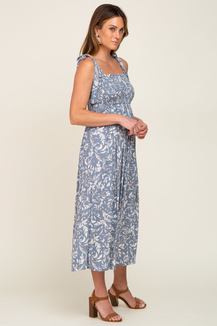 woman wearing a blue floral midi dress with spaghetti straps and a smocked bodice, standing in profile
