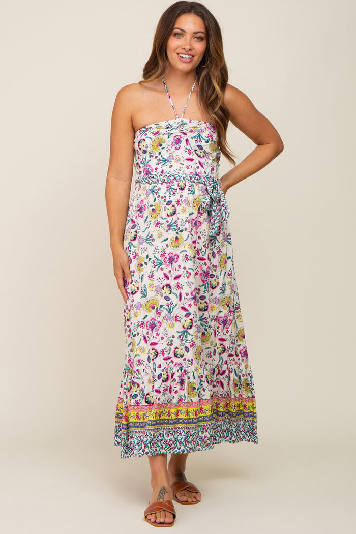 woman wearing a white floral halter neck maternity maxi dress with a belted waist and ruffled hem