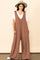 woman wearing a brown wide leg jumpsuit over a white t-shirt and a tan wide brim hat