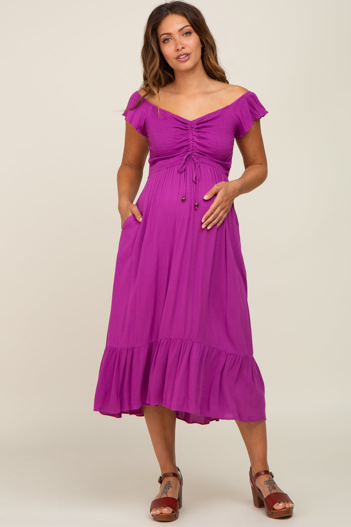 woman wearing a purple off-the-shoulder maternity dress with smocked bodice and ruffle hem, showcasing her baby bump