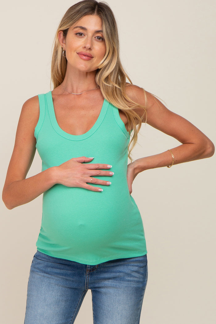 woman wearing a teal maternity tank top and holding her baby bump while posing in a relaxed manner