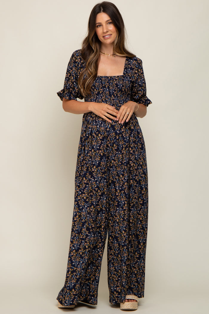 woman wearing a navy floral maternity jumpsuit with short sleeves and a square neckline, posing with a relaxed look