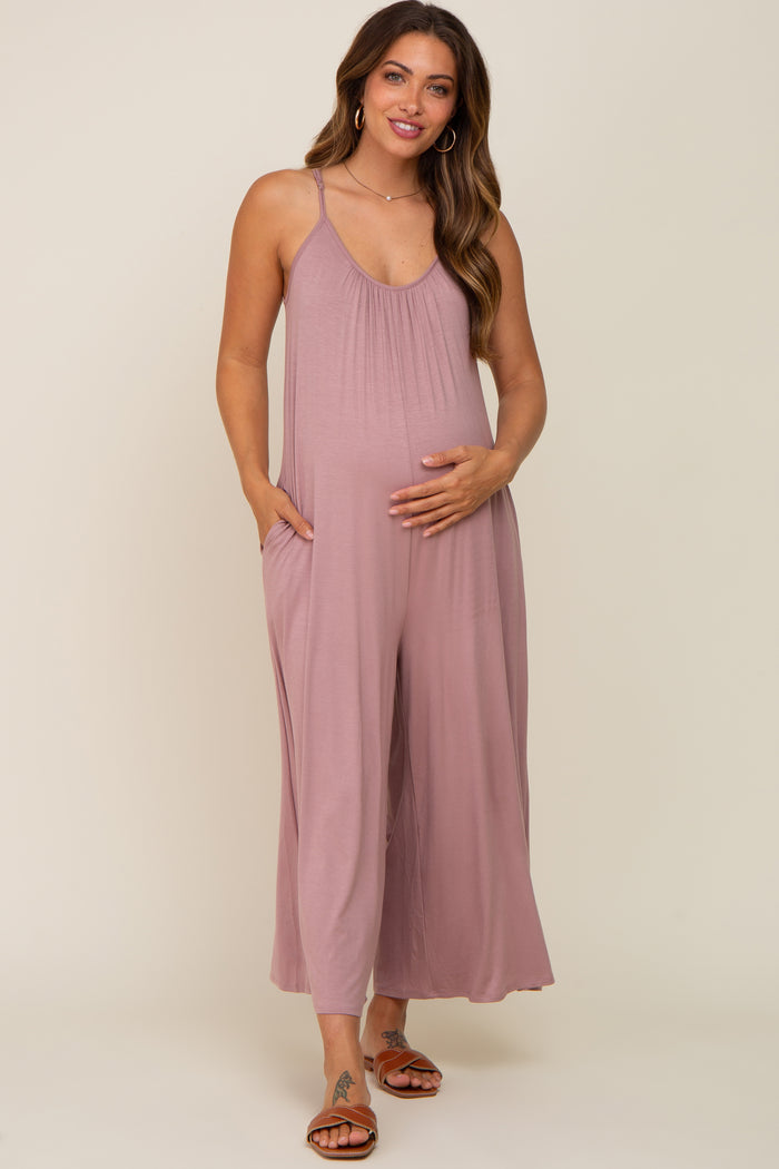 woman wearing a mauve sleeveless maternity jumpsuit with pockets and a visible baby bump, standing and smiling