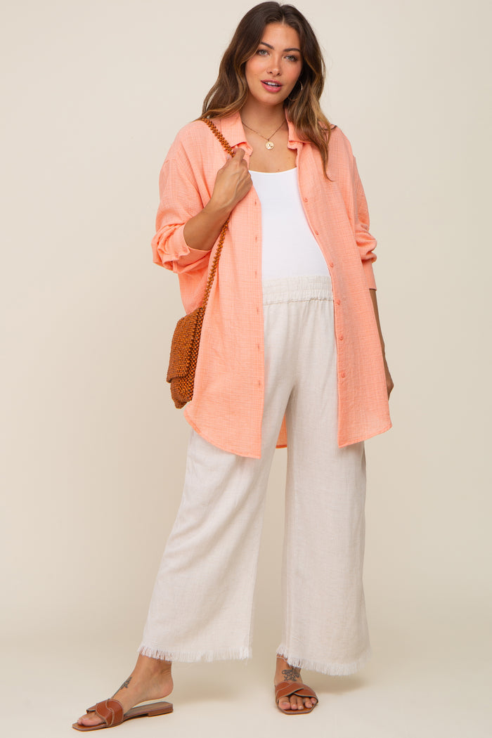Pregnant woman wearing a peach gauze button-down shirt, white tank top, and cream wide-leg linen pants