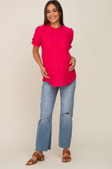 woman wearing a bright pink short sleeve maternity top and distressed light wash jeans, holding her baby bump