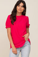 woman wearing a bright pink short sleeve blouse with a ruffled neckline and puff sleeves, paired with light blue jeans