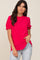 woman wearing a bright pink short sleeve blouse with a ruffled neckline and puff sleeves, paired with light blue jeans