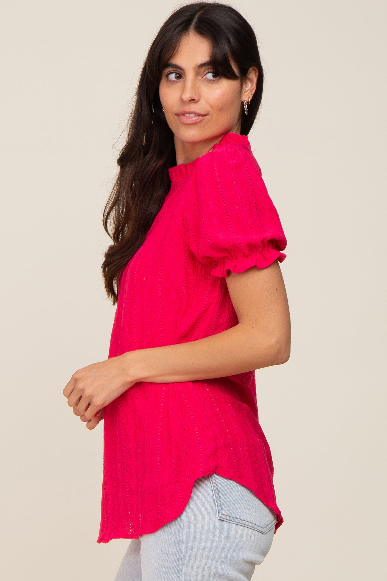 woman wearing a hot pink short sleeve top with puffed sleeves and a high-low hemline paired with light blue jeans