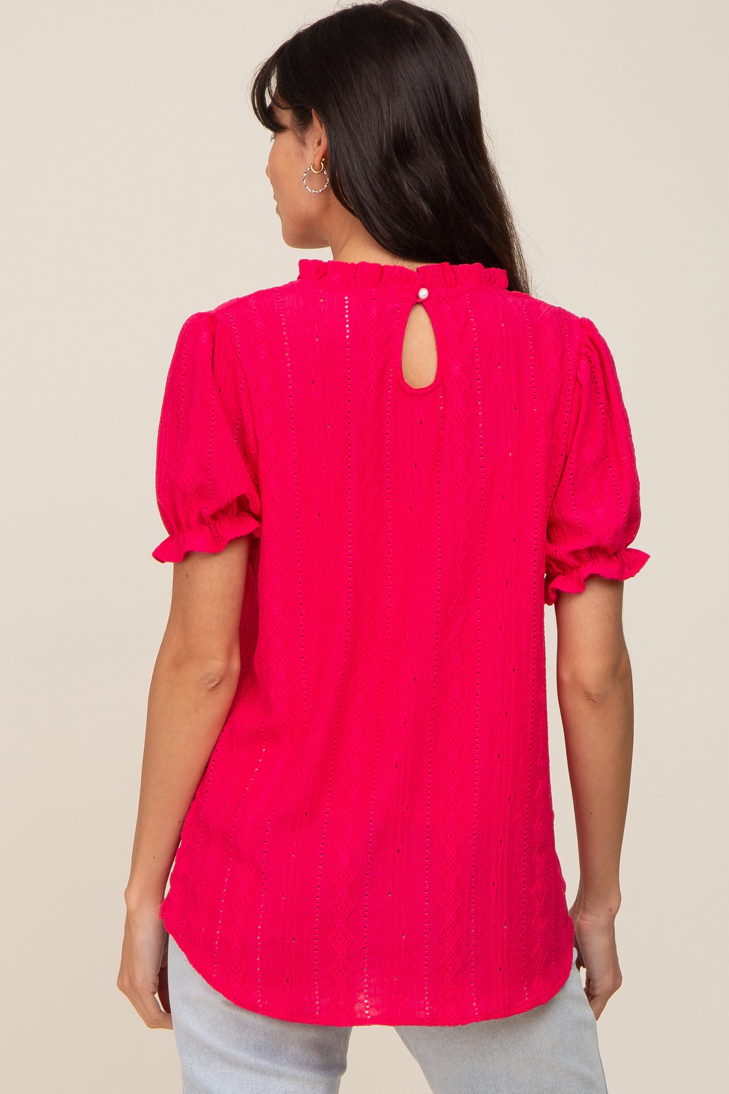 woman wearing a bright pink short sleeve blouse with a keyhole back and ruffle details