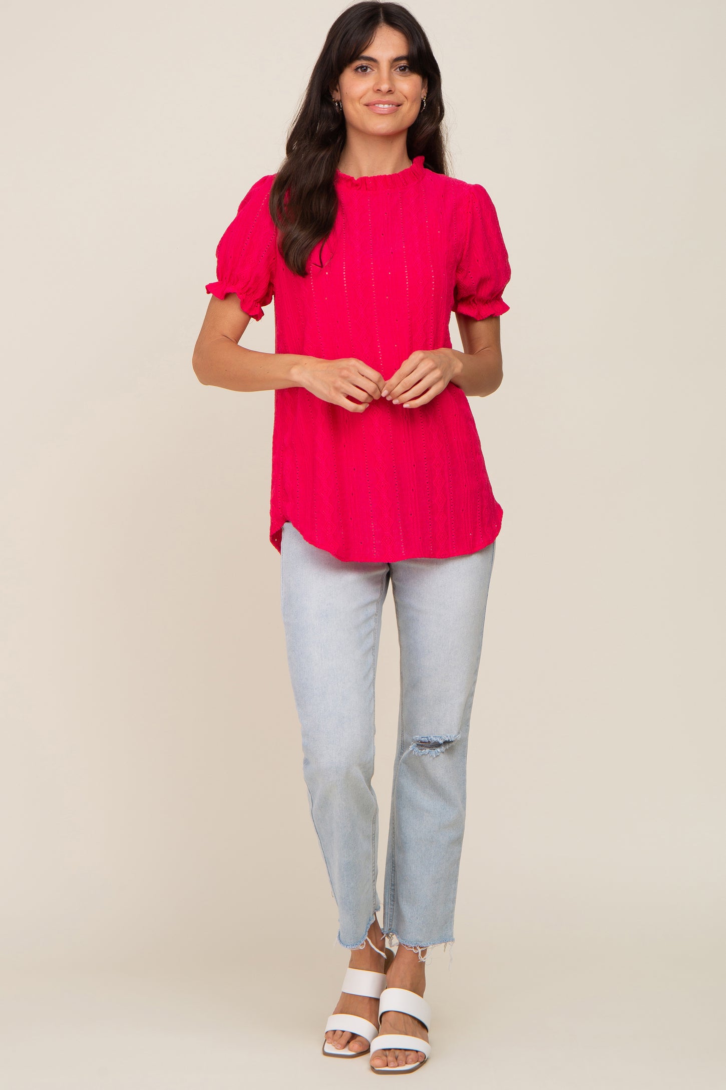 woman wearing a bright pink short sleeve top with textured details and accompanied by light blue ripped jeans and white block heels