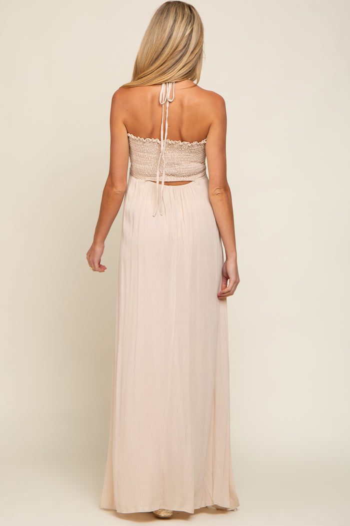 woman wearing a light peach maternity maxi dress with a smocked bodice and halter neckline, showing off her baby bump rear view