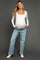 woman wearing a white long sleeve maternity top and blue jeans, showing her baby bump