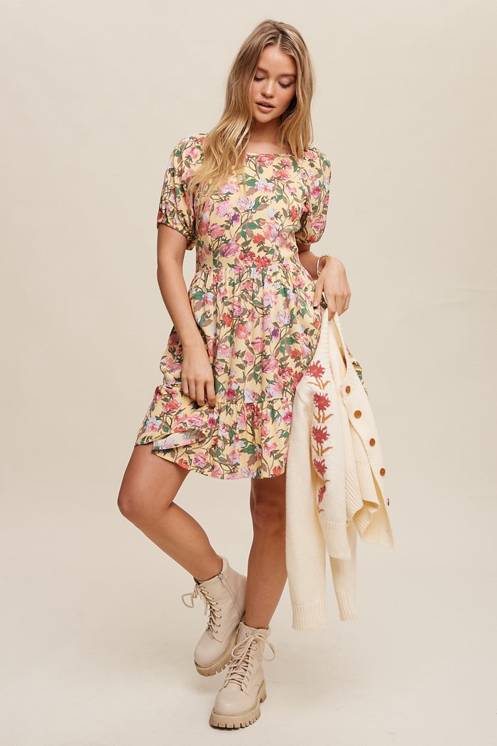 Woman wearing a yellow floral mini dress and beige combat boots holding a cream cardigan