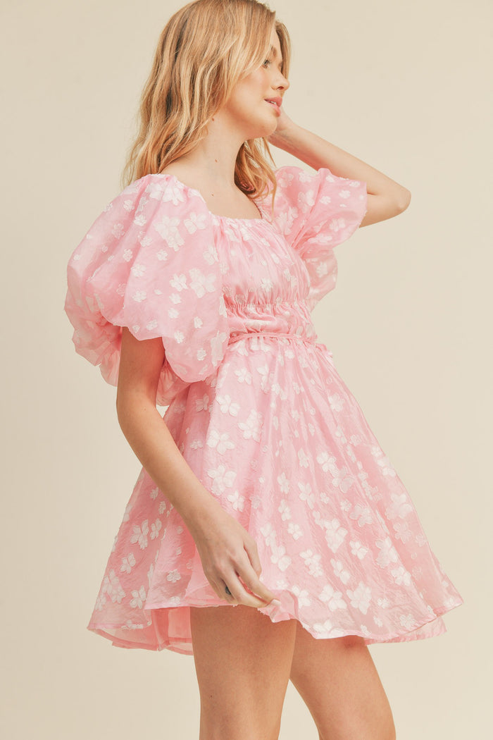 woman wearing a pink floral puff sleeve mini dress with a gathered waist and a flared skirt