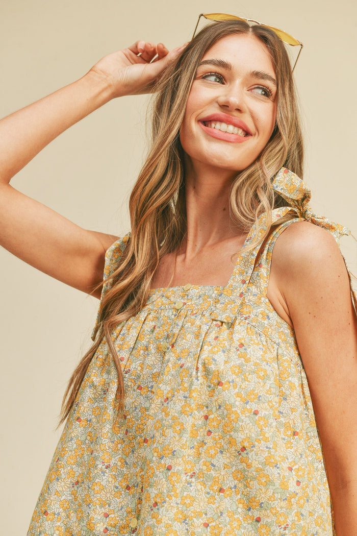 woman wearing a yellow floral print sleeveless top with tie straps and a relaxed fit