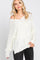 woman wearing an off-white oversized knit sweater with a scooped neckline and side slits, paired with black jeans