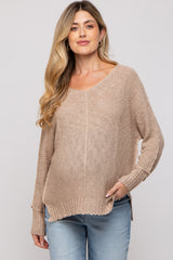 woman wearing a beige knitted maternity sweater with a v-neck and relaxed fit, styled with light blue jeans